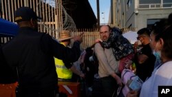 FILE - Ukrainian refugees speak with a U.S. Customs and Border Patrol official as they prepare to cross the border on April 4, 2022, in Tijuana, Mexico. The Biden administration on Aug. 18, 2023, announced an expansion of temporary legal status for Ukrainians living in the U.S.