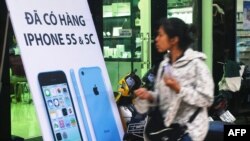 FILE - A woman walks past a shop selling latest Apple iPhones in downtown Hanoi on Sept. 26, 2013.