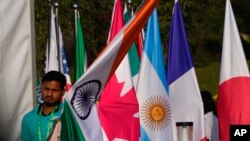 A worker carries Indian national flag to place it with those of other participating countries at the opening session of the G20 foreign ministers meeting, in New Delhi, India, March 2, 2023.