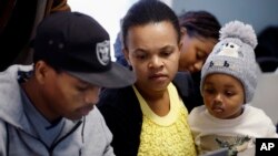 Richemene Bertrand, center, holds her daughter Jumaily Secius while learning computer skills with her husband, Jean Francois Secius, Dec. 22, 2023, in Boston. 