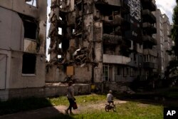 A woman and a boy make their way past an apartment building destroyed in Russian attacks in Borodyanka, Ukraine, Aug. 2, 2023.
