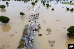 FILE - People walk through floodwaters after heavy rainfall in Hadeja, Nigeria, Sept 19, 2022. A new United Nations report on climate change is being held up by a battle between rich and developing countries over emissions targets and financial aid to vulnerable nations. (AP Photo, File)