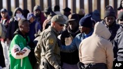 FILE - A member of US Customs and Border Protection tries to control a group of migrants as hundreds gather along the border after breaking through gaps in the border wall Dec. 5, 2023, in Lukeville, Ariz. 