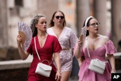 FILE - Tourists use foldable fans to cool off as they visit Rome, July 22, 2023.
