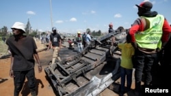 People stand next to a police vehicle that was burned during a demonstrations against the Kenya's proposed finance bill in Nairobi, Kenya, June 26, 2024. 
