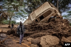 Seorang pria berjalan di dekat mobil yang rusak di daerah yang terkena dampak hujan lebat dan banjir bandang di desa Kamuchiri, dekat Mai Mahiu, 29 April 2024.(LUIS TATO / AFP)