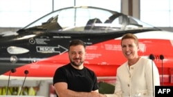 资料照：2023年8月20日，乌克兰总统泽连斯基（左）和丹麦首相梅特·弗雷德里克森在丹麦北部一处空军基地的一架F-16战斗机前握手。（法新社）