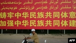 FILE - This picture taken July 17, 2023, shows a man riding a scooter past a government billboard urging people to 'forge an understanding of the collective Chinese people' outside Yarkant in northwestern China's Xinjiang region.