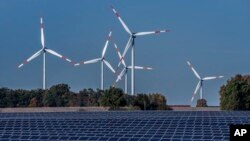 FILE - Wind turbines turn behind a solar farm in Rapshagen, Germany, Oct. 28, 2021.