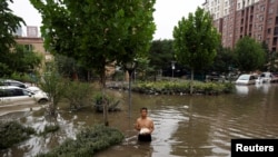 资料照：河北涿州一名男子手拿食物走在积满洪水的街道上。（2023年8月3日）