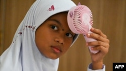 Seorang murid sekolah dasar menggunakan kipas portabel untuk mengusir hawa panas saat belajar di kelas, di Banda Aceh, Aceh, 15 Mei 2023. (Foto: Chaideer Mahyuddin/AFP)