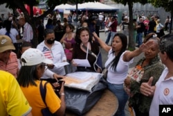 A woman tries to maintain order before to open a polling station during primary election at the Luis Brion square in Caracas, Venezuela, Oct. 22, 2023.