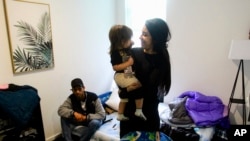 FILE - Barbara Peraza-Garcia holds her 2-year-old daughter, Frailys, while her partner, Franklin Peraza, sits on their bed in their 'micro apartment' in Seattle on March 11, 2024. 
