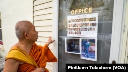 พระครูอุดม อุตฺตมสีโล เจ้าอาวาสวัดญาณรังษี มองดูแผ่นประกาศของตำรวจที่เผยแพร่โฉมหน้าคนร้ายแก๊งอาชญากรชาวโรมาเนียที่ตำรวจต้องการตัว ติดอยู่บริเวณทางเข้าสำนักงานวัดญาณรังษี เมืองสเตอร์ริง รัฐเวอร์จิเนีย