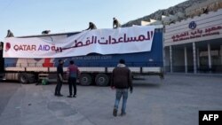 Men stand next to a truck, part of a convoy carrying aid provided by Qatar, in the aftermath of an earthquake, at Syria's Bab al-Hawa border crossing with Turkey in the rebel-held northwestern province of Idlib, on February 13, 2023.