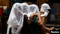 Para pria mengendarai sepeda motor sambil menutupi kepala mereka dengan kain basah untuk mendinginkan dan menghindari sinar matahari saat gelombang panas terus berlanjut di Jacobabad, Pakistan, 26 Mei 2024. (Foto: Reuters)