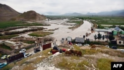 Warga Afghanistan berkumpul di sepanjang jalan menuju daerah banjir antara Samangan dan Mazar-i-Sharif menyusul banjir bandang yang disebabkan oleh hujan lebat di distrik Feroz Nakhchir, Provinsi Samangan pada 11 Mei 2024. (Foto: AFP)