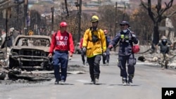 Members of a search-and-rescue team walk along a street, Aug. 12, 2023, in Lahaina, Hawaii, following heavy damage caused by wildfire.