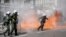 A riot police officer prepares to throw a stun grenade next to flames as clashes take place during a demonstration following the collision of two trains, near the city of Larissa, in Athens, March 5, 2023. 