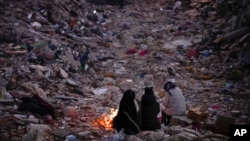 FILE - Members of a family keep warm next to a fire as they follow a rescue team searching for their relatives among destroyed building in Antakya, southern Turkey, Feb. 15, 2023.