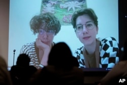 Jenya Polosina, left, Anna Ivanenko, right, both Kyiv, Ukraine-based artists, appear from Kyiv via video link on a screen at an art opening for an exhibit called "Our Fire is Stronger Than Your Bombs" at Saint Anselm College in Manchester, N.H., Monday, May 1, 2023. (AP Photo/Steven Senne)