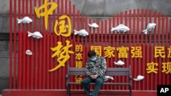 资料照：一名戴着口罩的男子在武汉街头一个中国梦的政府宣传牌下打盹。（2020年4月8日）