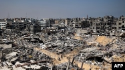 FILE - People walk amid the rubble of destroyed buildings in Khan Yunis, Gaza Strip, on April 16, 2024. Rubble throughout Gaza is probably contaminated with unexploded ordnance, say landmine and explosives experts at a U.N. conference in Geneva on May 1, 2024.
