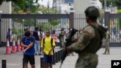Students walk past soldiers standing guard inside a school in downtown Guayaquil, Ecuador, Aug. 18, 2023.