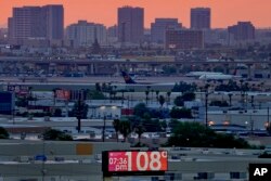 FILE - A sign displays an unofficial temperature as jets taxi at Sky Harbor International Airport at dusk, July 12, 2023, in Phoenix.
