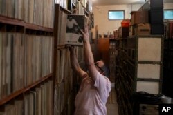 Carlos Savalla mengembalikan sejumlah album ke rak di studionya tempat ia menyimpan koleksi musiknya, di Rio de Janeiro, Brazil, Jumat, 19 April 2024. Savalla, seorang produser musik berusia 66 tahun di Rio, memiliki lebih dari 60.000 piringan hitam. (AP/Bruna Prado)