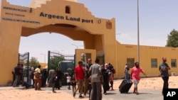 Evacuees carry their luggage as they cross into Egypt through the Argeen land port after being evacuated from Sudan to escape the conflict, on the international border lines between Egypt and Sudan, April 27, 2023.