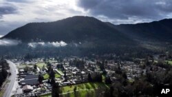 A vehicle at left drives down Rogue River Highway as light shines on the area, March 23, 2024, in Grants Pass, Ore. 