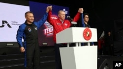 In this photo released by the Turkish Presidency, President Recep Tayyip Erdogan, center, holds up the hands of Turkish air force pilot Alper Gezeravci, left, and aviation systems engineer Tuva Cihangir Atasever at Teknofest military fair, in Istanbul, April 29, 2023. 
