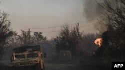 14일 우크라이나 동부 격전지 바흐무트 인근 상공에서 폭발이 발생한 직후 나무가 불타고 있는 가운데 우크라이나 군용 차량이 이동하고 있다. 