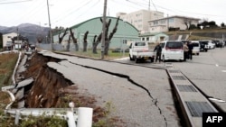 Orang-orang berdiri di dekat retakan besar di trotoar setelah mengungsi ke jalan di kota Wajima, prefektur Ishikawa pada 1 Januari 2024, setelah gempa bumi besar berkekuatan 7,5 melanda wilayah Noto di prefektur Ishikawa. (Foto: AFP)