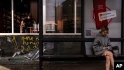 A commuter waits for a bus in front of a liquor store damaged in Russian drone attacks in Kyiv, Ukraine, Aug. 2, 2023.