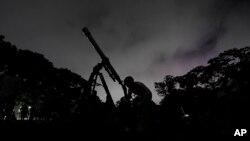 FILE - A girl looks at the moon through a telescope in Caracas, Venezuela, May 15, 2022. Mercury, Jupiter, Venus, Uranus and Mars will gather near the moon in a planet parade this week. The best day to catch the whole group will be Tuesday after sunset.