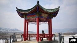 A woman sitting on a bench looking at Chunggang County North Korea in Linjiang in the province of Jilin, northeast China, Feb. 29, 2024.
