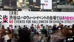 Orang-orang menunggu di depan papan bertuliskan "Tidak ada acara Halloween di jalan-jalan Shibuya" di Shibuya Crossing di distrik Shibuya, Tokyo, 27 Oktober 2023. Pemerintah setempat meminta masyarakat untuk tidak merayakan Halloween di sana. (Philip FONG / AFP)