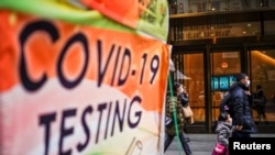 People wearing masks walk next to a COVID-19 testing site in New York City, December 12, 2022.