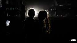 A Palestinian girl holding a child is silhouetted in against the lights of an oncoming car in Rafah, in the southern Gaza Strip, on May 4, 2024.