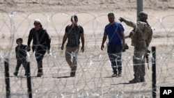 FILE - Migrants wait for U.S. authorities, between a barbed-wire barrier and the border fence at the U.S.-Mexico border, as seen from Ciudad Juarez, Mexico, May 10, 2023.