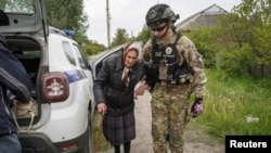 A police officer helps a local resident during an evacuation due to Russian shelling, amid Russia's attacks on Ukraine, in the town of Vovchansk in Ukraine's Kharkiv region, May 13, 2024. 