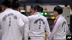 North Korean women wearing track suits with the North Korean flag hold hands as they line up to check in for a flight to Astana, Kazakhstan, at the Capital Airport in Beijing, Aug. 18, 2023. 