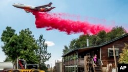 FILE - A woman watches an air tanker drop retardant as the Electra Fire burns towards her home in Amador County, California, on July 5, 2022. 
