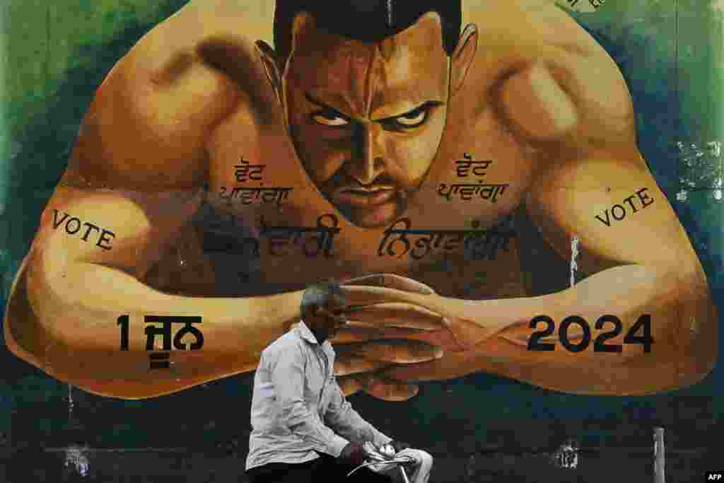 Seorang pria mengendarai sepeda melewati mural yang menggambarkan aktor Bollywood Aamir Khan dan slogan-slogan untuk mendorong masyarakat memberikan suara mereka, di Jalandhar, menjelang pemungutan suara tahap keempat dalam pemilihan umum India.