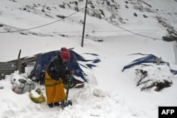 Seorang perempuan membersihkan salju di depan kediamannya di Sela Pass, negara bagian Arunachal Pradesh, India, 2 April 2023. (Arun SANKAR/AFP)
