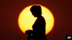 FILE - A woman is silhouetted against the setting sun, Aug. 1, 2022, in Kansas City, Missouri. Biases against women has shown no progress over the past decade, according to a United Nations report.