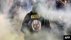 A protester wearing a garment depicting the Israeli prime minister walks through smoke as relatives and supporters of Israelis taken hostage by Palestinian militants in Gaza in the October 7 attacks demonstrate in Tel Aviv on May 26, 2024