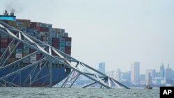 The Baltimore city skyline is visible behind a cargo ship that is stuck under part of the structure of the Francis Scott Key Bridge after the ship hit the bridge, March 26, 2024, in Baltimore.